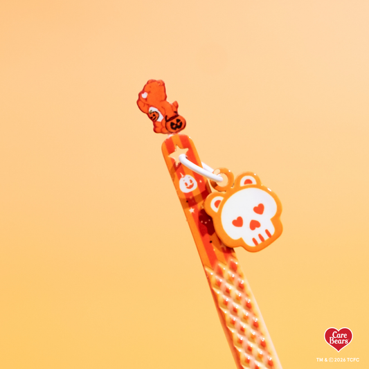 Élan Beauté x Care Bears orange Halloween lash tweezer featuring a textured grip, Care Bear topper, and dangling skull charm against a warm orange background.