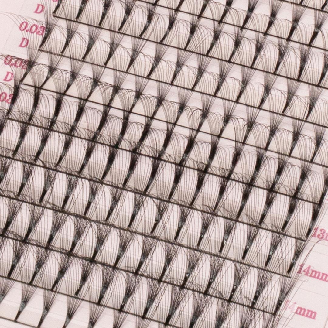 Close-up of premade volume lash fans arranged in rows on a pink tray, showing fine black fibers and pointed bases.