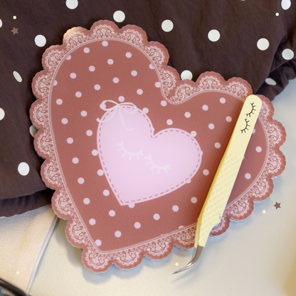 Lace Heart Lash Tile in brown with pink polka dots with yellow tweezers laying on it. 