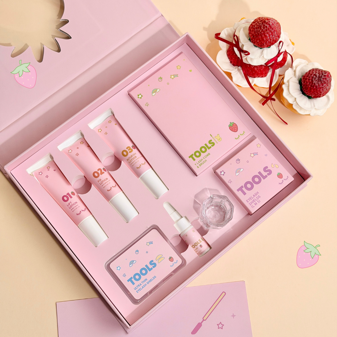 View of 01 Lift Lotion, 02 Fix Lotion, 03 Nourish lotion, eyelash shields, Y lash comb and brush, and glue in its pink box with strawberry pastries next to it.