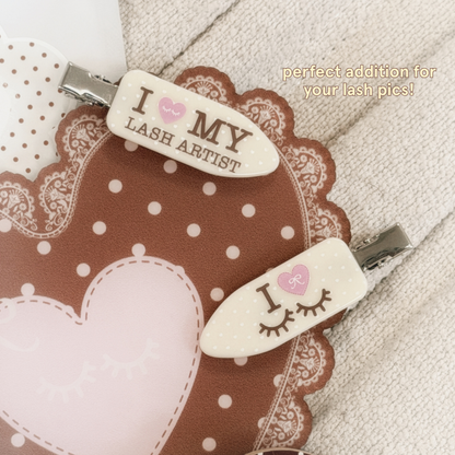 Crease-free hair clips with yellow and white polka dots and text on it saying "I Heart My Lash Artist" in brown text and the other clip saying "I Heart Eyelashes" and text saying "Perfect addition for your lash pics!"