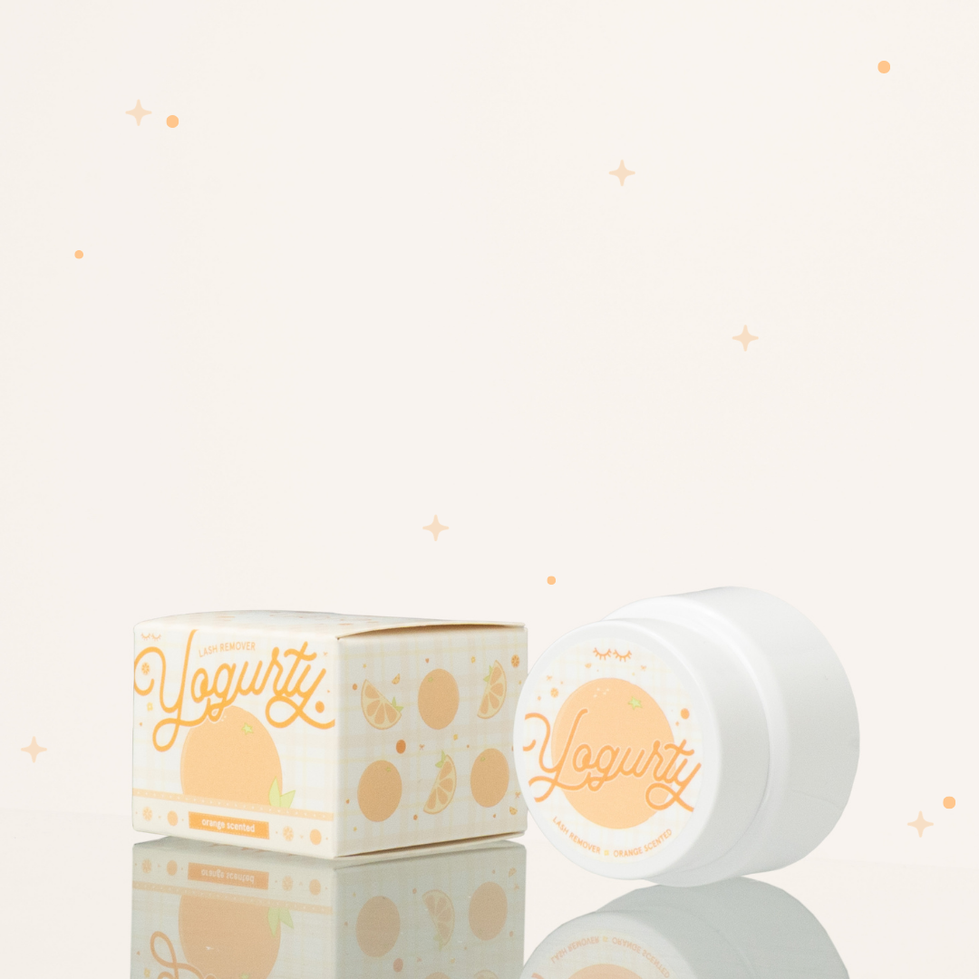 Side view of orange scented yogurty lash remover beside its orange-and-white packaging with orange illustrations on it.