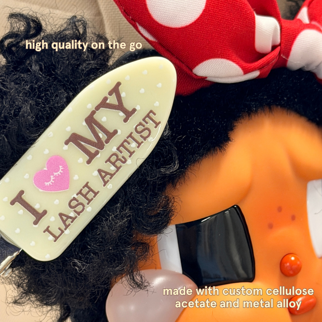 Crease-free hair clips with yellow and white polka dots and text on it saying "I Heart My Lash Artist" in brown text with text saying "High quality on the go" and "Made with custom cellulose acetate and metal alloy"