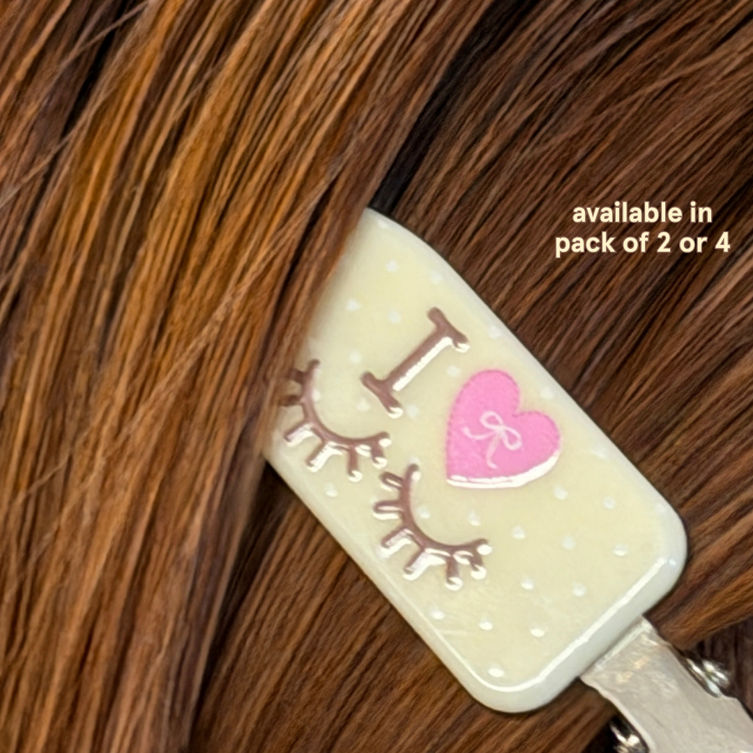 Crease-free hair clips with yellow and white polka dots and text on it saying "I Heart Lashes" in brown text. Text in yellow font saying "Available in pack of 2 or 4"