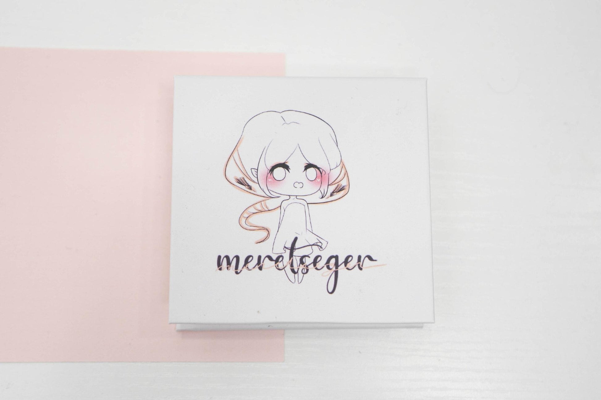 Meretseger false eyelash box featuring an illustrated character on a white and pale pink background.