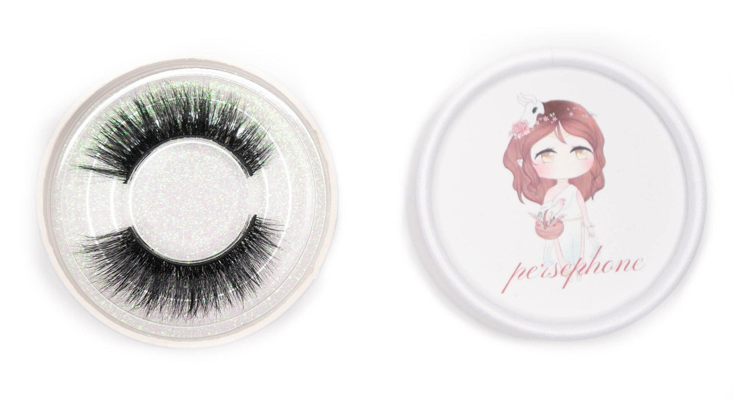 Persephone false eyelashes in a clear round case beside the illustrated Persephone product lid on a white background.