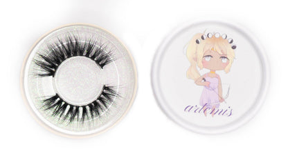 Artemis false eyelashes in a clear round case beside the illustrated Artemis product lid on a white background.