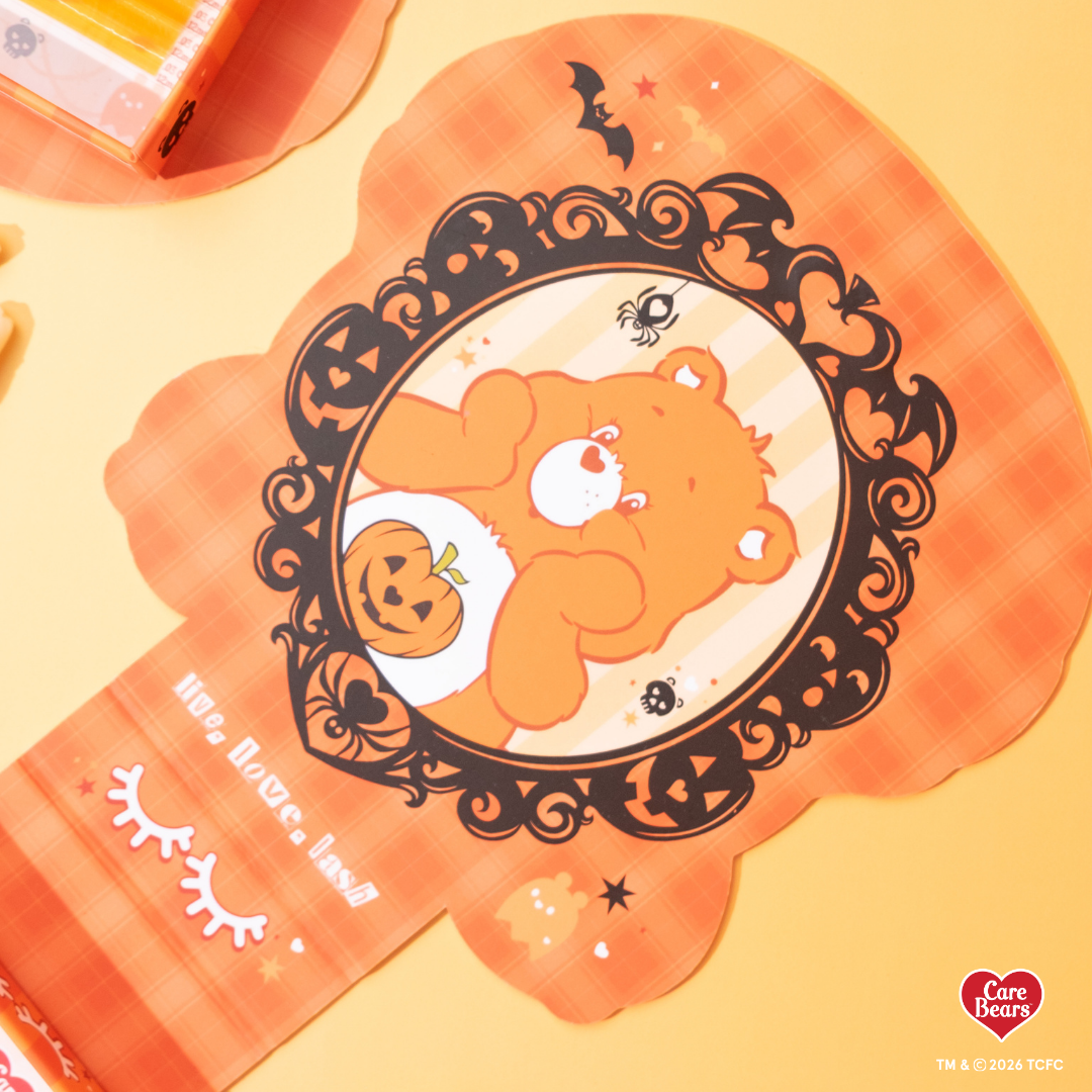 Élan Beauté x Care Bears Halloween packaging featuring an orange Care Bear holding a jack-o’-lantern, framed by black bats, pumpkins, spiders, and gothic Halloween details on an orange background.