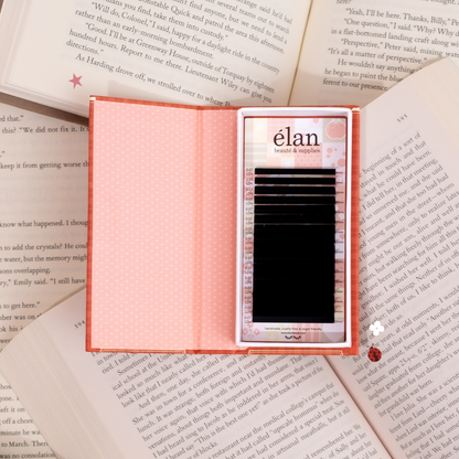 Open Comic Lashes tray displayed like a book, featuring black lash extensions inside red and pink packaging, styled on top of open book pages.