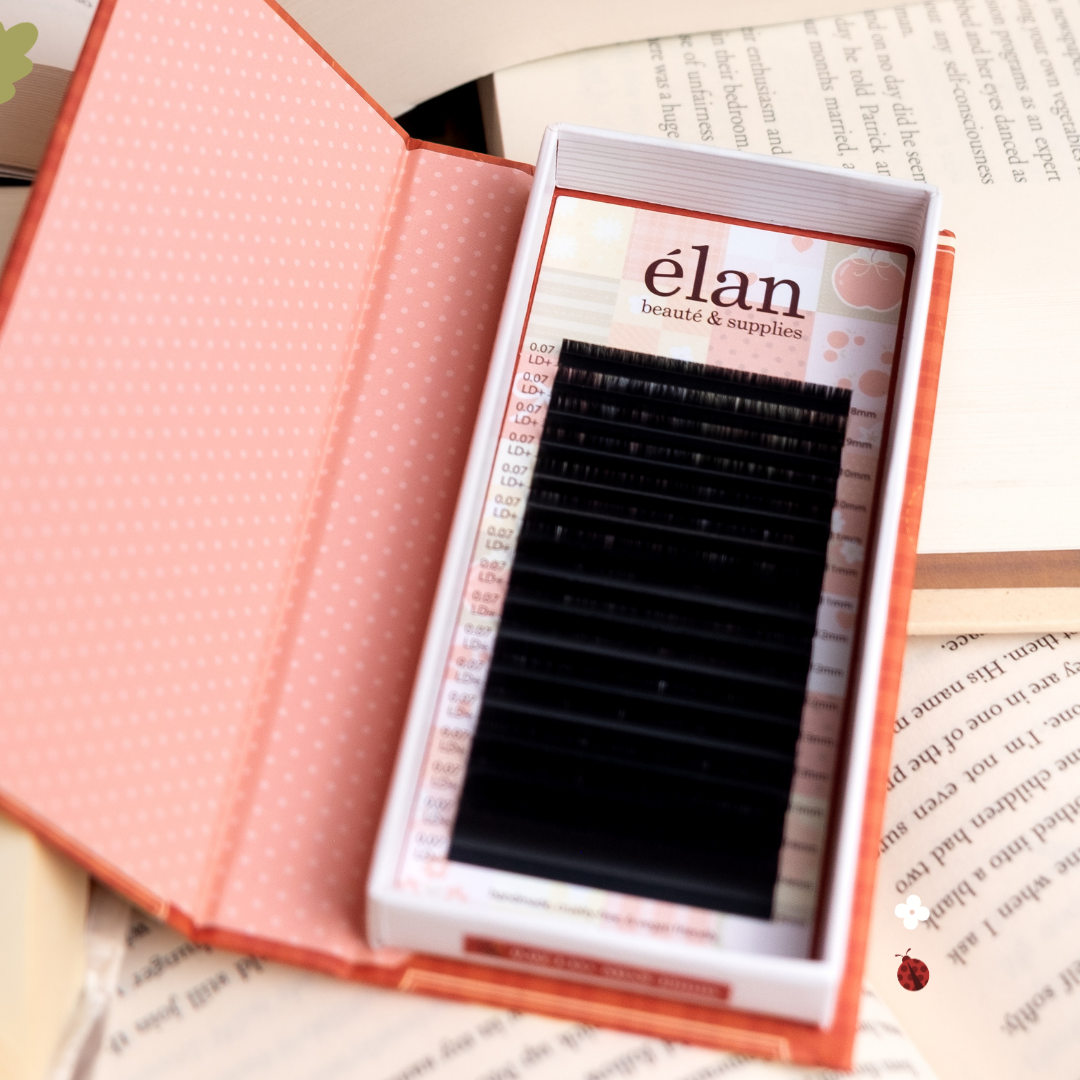 Open Comic Lashes tray displayed like a book, featuring black lash extensions inside red and pink packaging, styled on top of open book pages.