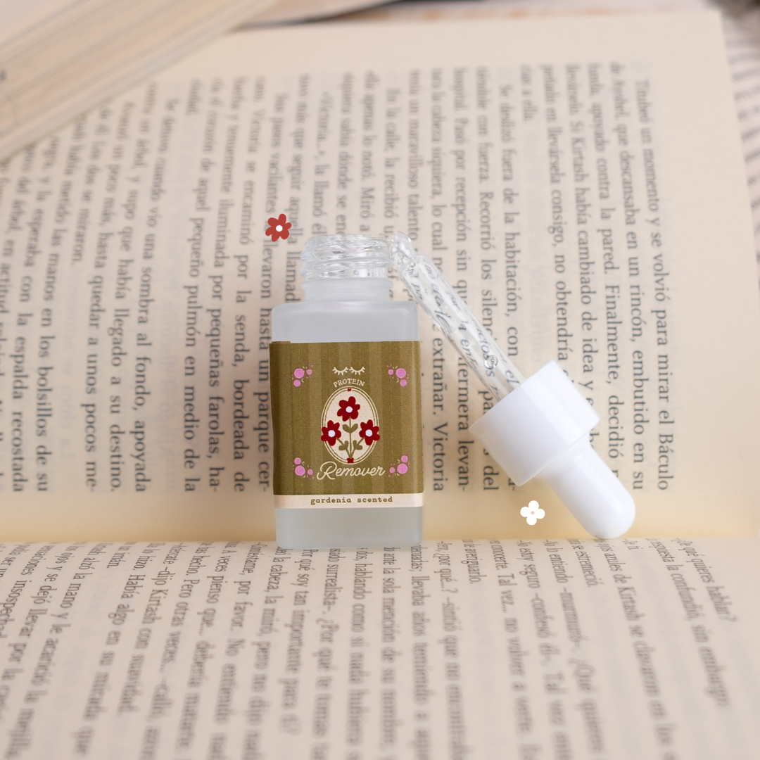 Gardenia-scented protein remover bottle shown open with its dropper beside it, styled on top of open book pages with small floral accents.