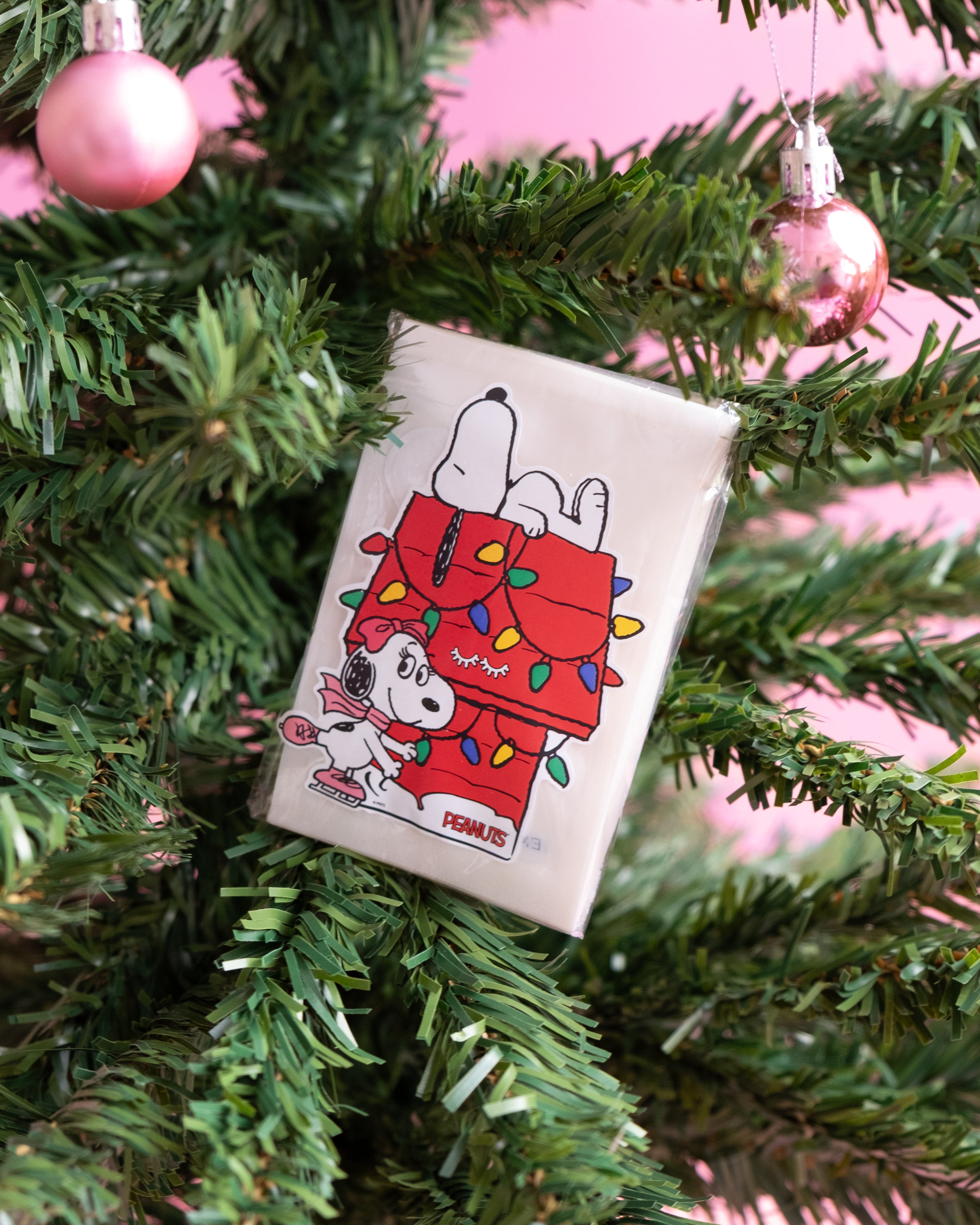 PEANUTS x Élan Beauté holiday decal set featuring Snoopy and Belle with Christmas lights, displayed on a Christmas tree with pink ornaments.