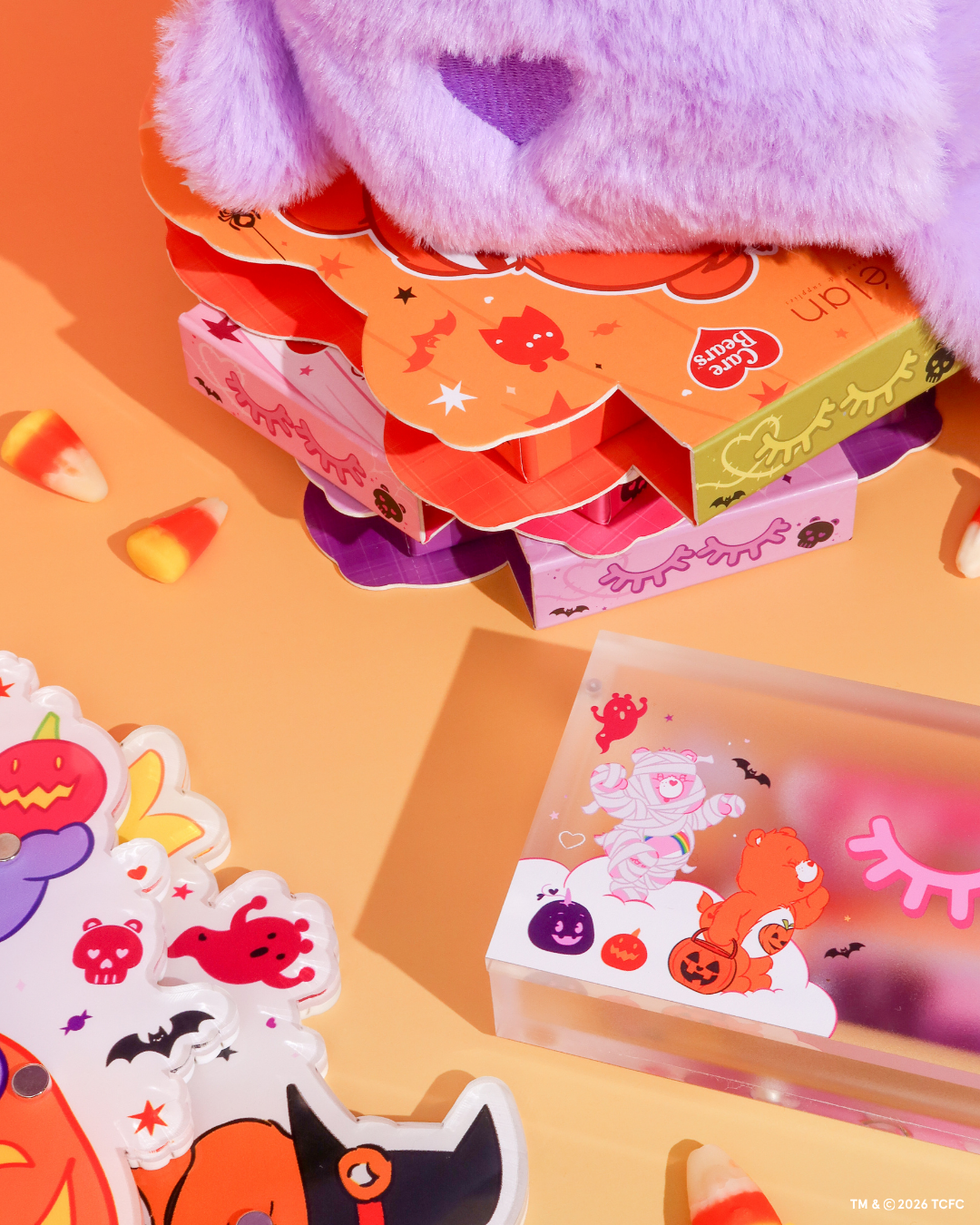 Élan Beauté x Care Bears Halloween collection featuring character-themed lash trays, XL lash tiles, and a magnetic tweezer case styled with a purple Care Bear plush and candy corn on an orange background.