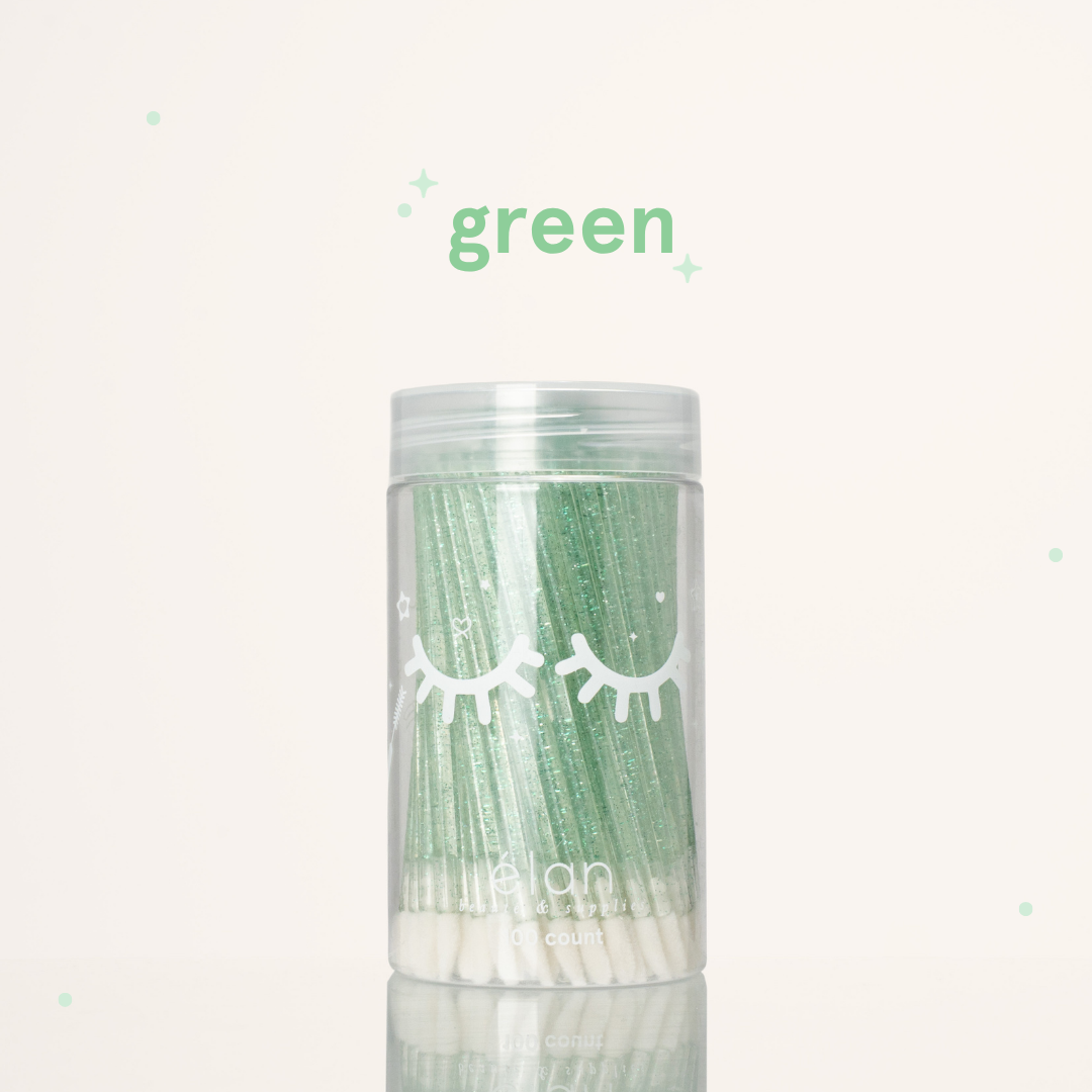 Élan Beauté green glitter lash applicator brushes in a clear 100-count container with white eyelash graphics, displayed on a soft cream background with green accents.