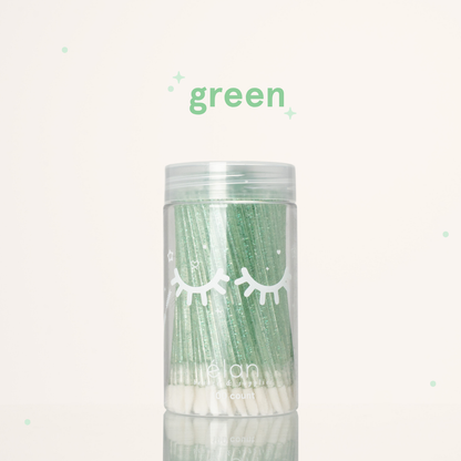 Élan Beauté green glitter lash applicator brushes in a clear 100-count container with white eyelash graphics, displayed on a soft cream background with green accents.