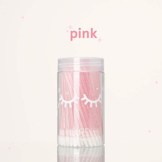 Élan Beauté pink glitter lash applicator brushes in a clear 100-count container with white eyelash graphics, displayed on a soft cream background with pink accents.