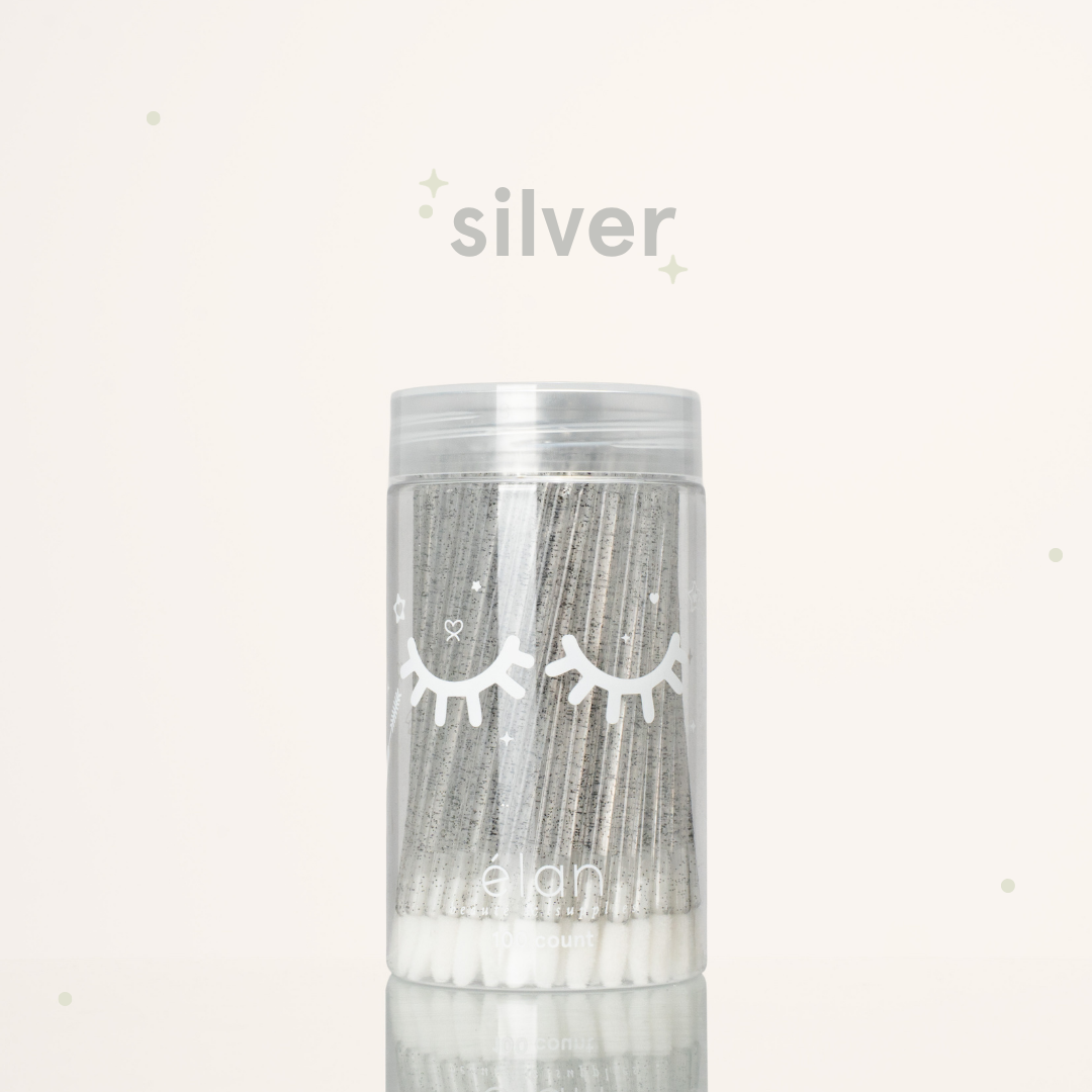 Élan Beauté silver glitter lash applicator brushes in a clear 100-count container with white eyelash graphics, displayed on a soft cream background with silver accents.