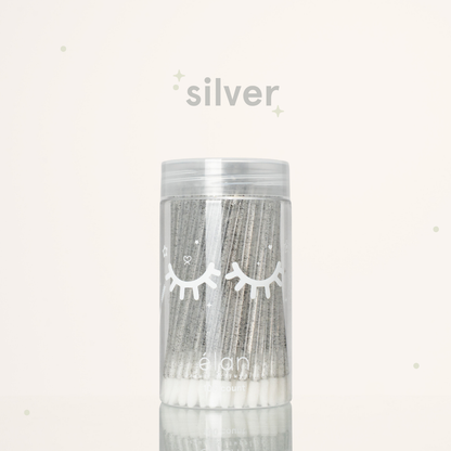 Élan Beauté silver glitter lash applicator brushes in a clear 100-count container with white eyelash graphics, displayed on a soft cream background with silver accents.