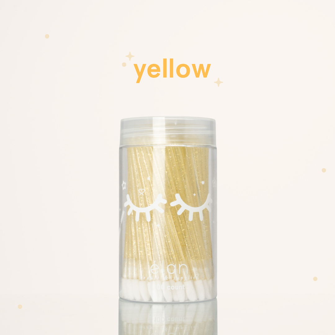 Élan Beauté yellow glitter lash applicator brushes in a clear 100-count container with white eyelash graphics, displayed on a soft cream background with yellow accents.