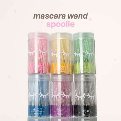 Mascara wand spoolies in clear containers, featuring glittery pink, yellow, green, blue, purple, and black handles with spoolie tips.