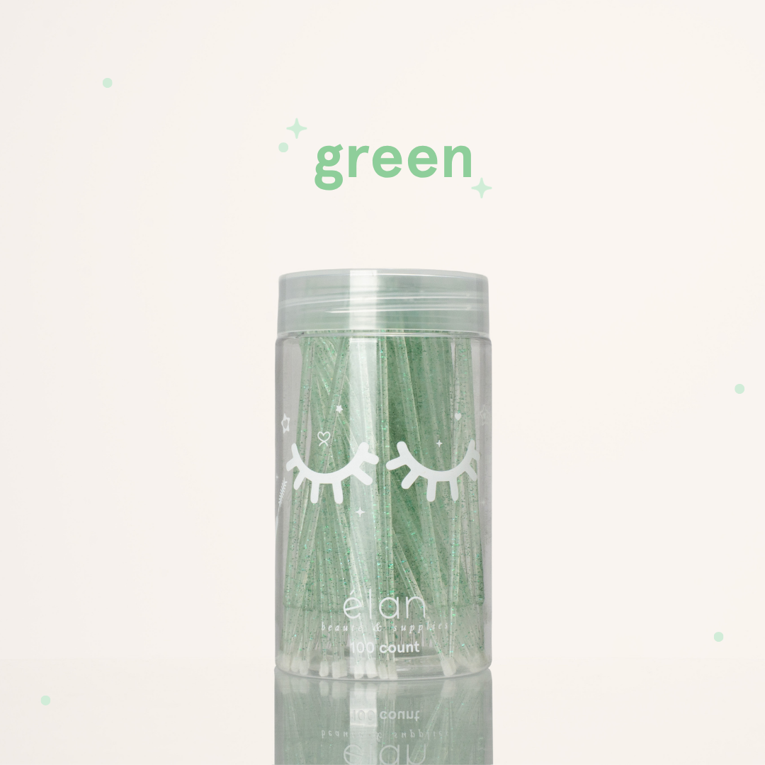 Élan Beauté green glitter microbrush applicator brushes in a clear 100-count container with white eyelash graphics, displayed on a soft cream background with green accents.