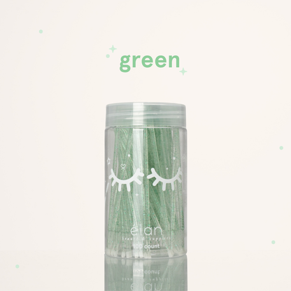 Élan Beauté green glitter microbrush applicator brushes in a clear 100-count container with white eyelash graphics, displayed on a soft cream background with green accents.