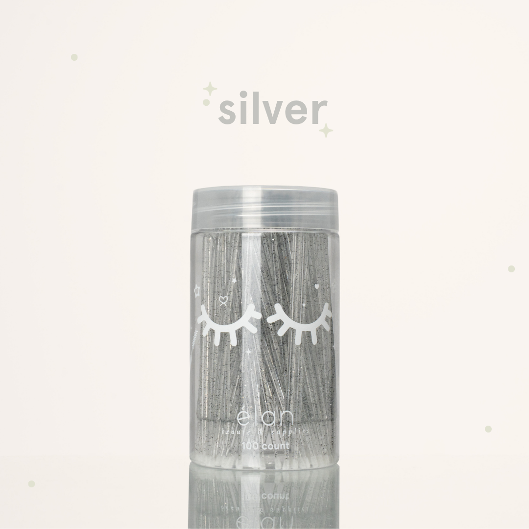 Élan Beauté silver glitter microbrush applicator brushes in a clear 100-count container with white eyelash graphics, displayed on a soft cream background with silver accents.