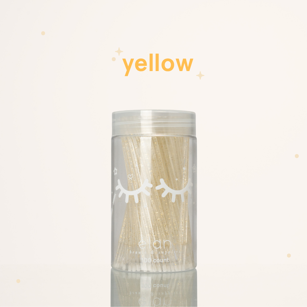 Élan Beauté yellow glitter microbrush applicator brushes in a clear 100-count container with white eyelash graphics, displayed on a soft cream background with yellow accents.