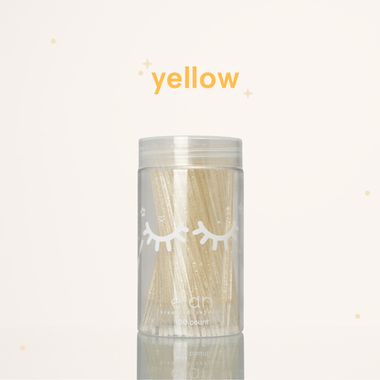 Élan Beauté yellow glitter microbrush applicator brushes in a clear 100-count container with white eyelash graphics, displayed on a soft cream background with yellow accents.
