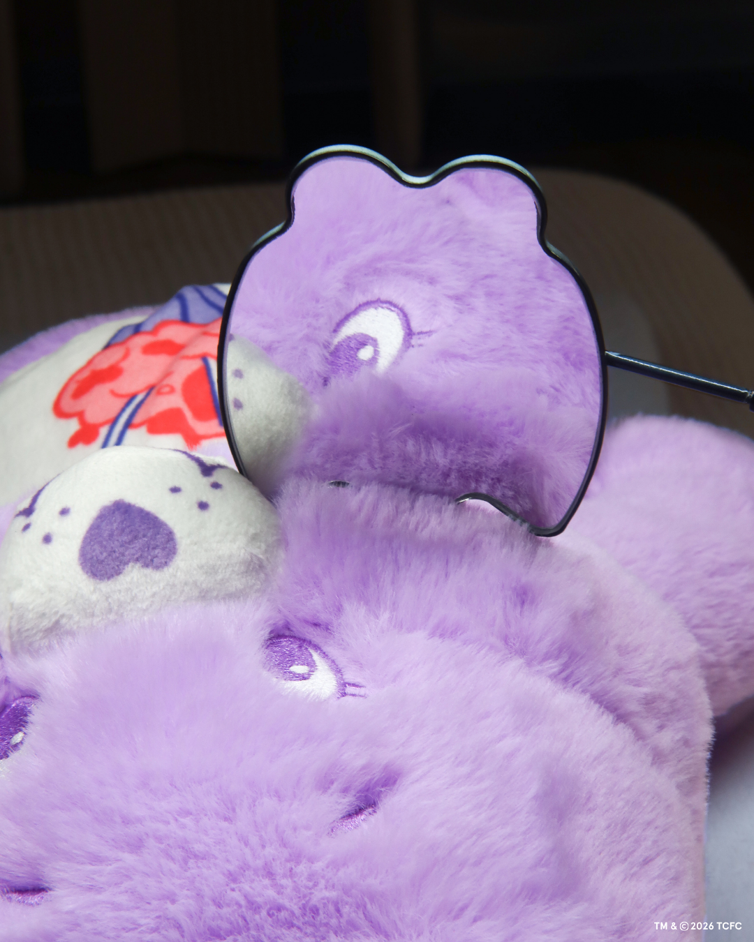 Élan Beauté x Care Bears handheld lash undereye mirror reflecting a purple Care Bear plush, styled with additional purple Care Bears plush toys in the background.