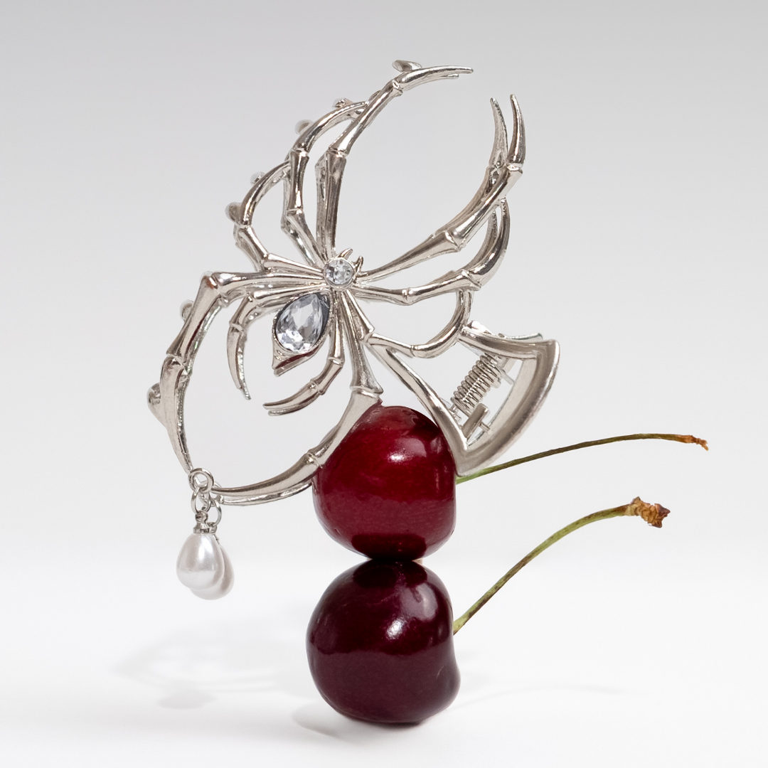 Spider hair claw clip featuring a silver spider design with crystal accents, styled around red cherries and pearl details on a clean white background.