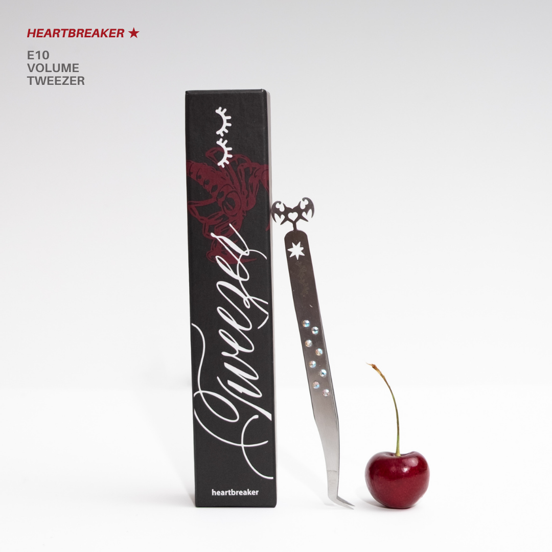 Heartbreaker E10 volume tweezer featuring a curved silver design with rhinestone accents, flame-shaped detailing, matching black rose-themed packaging, and a red cherry on a white background.