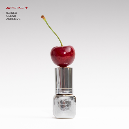 Angel Babe 0.3-second clear lash adhesive in a reflective silver bottle, topped with a red cherry and photographed on a clean white background.