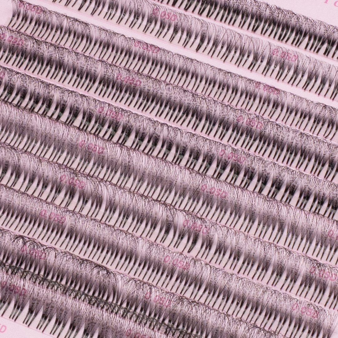 Close-up of rows of premade lash fans arranged on a pink lash tray, showing dense, evenly spaced black lash clusters.