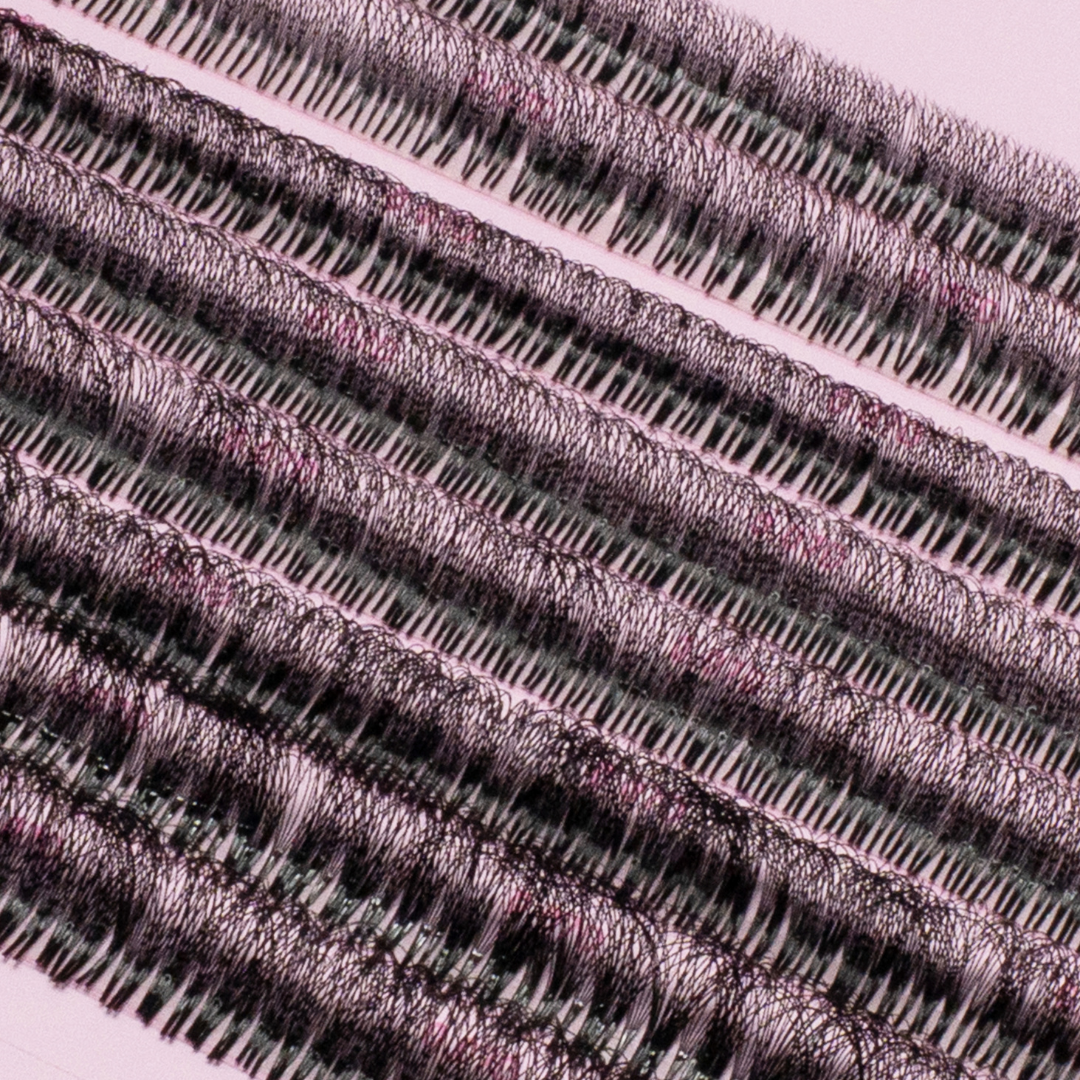 Close-up of rows of premade lash fans arranged on a pink lash tray, showing dense, evenly spaced black lash clusters.