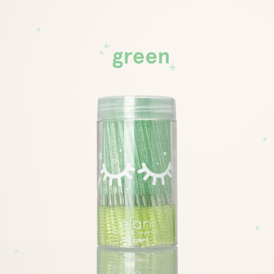 Élan Beauté green glitter spoolies in a clear 100-count container with white eyelash graphics, displayed on a soft cream background with green accents.