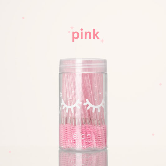 Élan Beauté pink glitter spoolies in a clear 100-count container with white eyelash graphics, displayed on a soft cream background with pink accents.