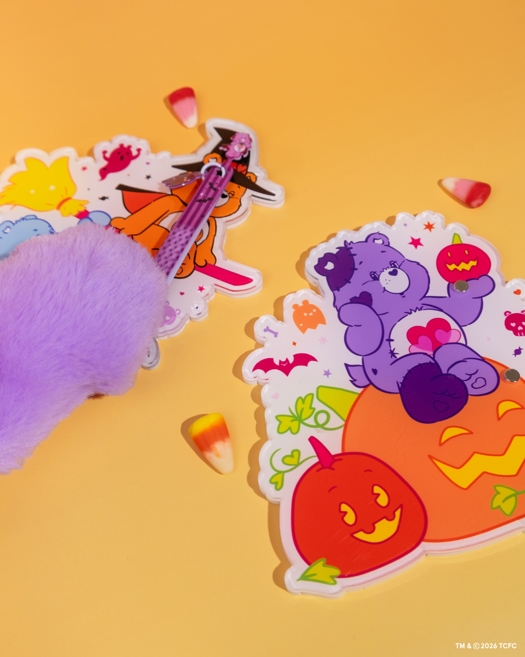 Élan Beauté x Care Bears Halloween XL lash tiles featuring Witch’s Broom and Jack-o’-Lantern designs, styled with a purple tweezer, plush Care Bear paw, and candy corn on a warm orange background.