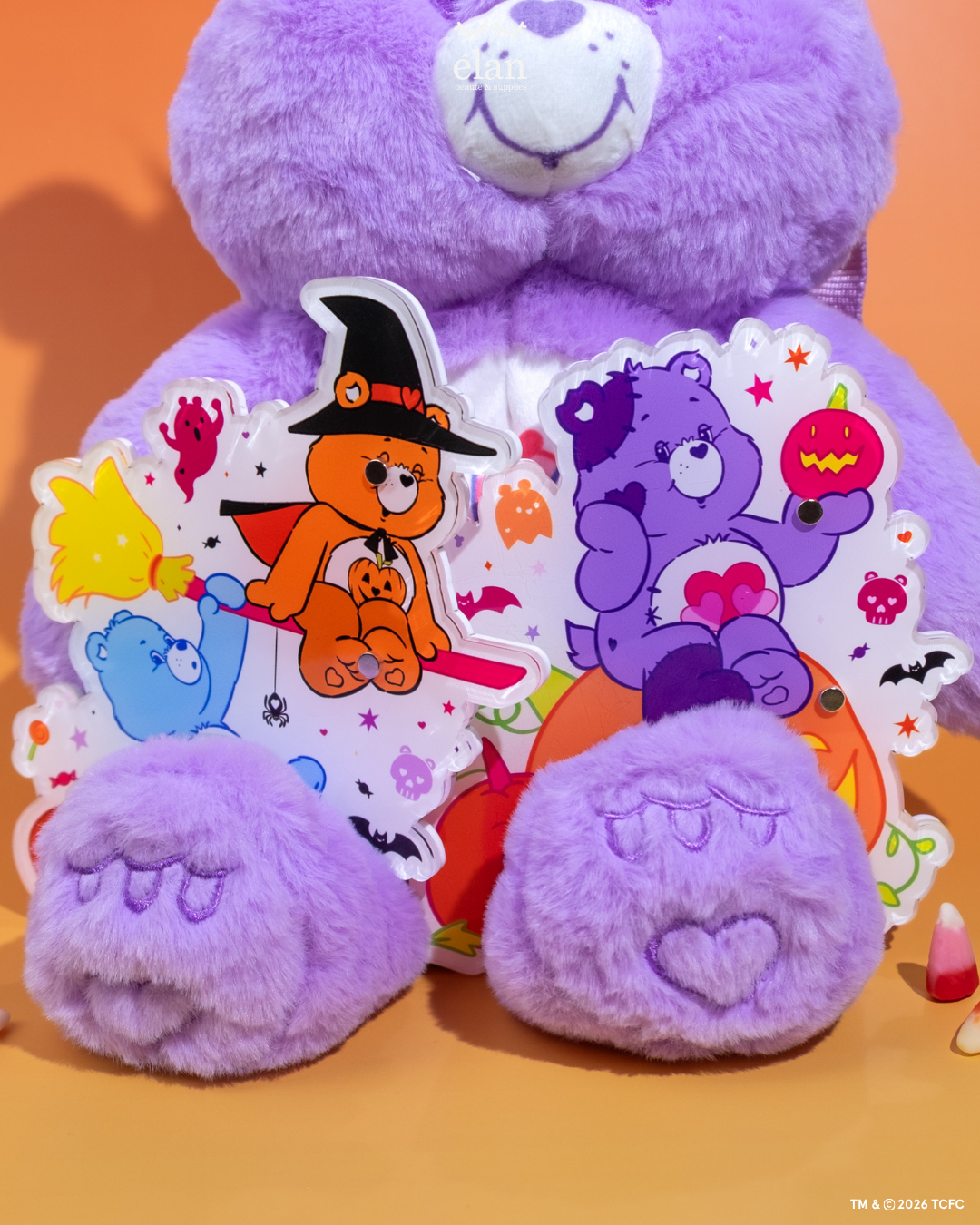 Élan Beauté x Care Bears Halloween XL lash tiles featuring Witch’s Broom and Jack-o’-Lantern designs, displayed with a purple Care Bear plush and candy corn accents on an orange background.
