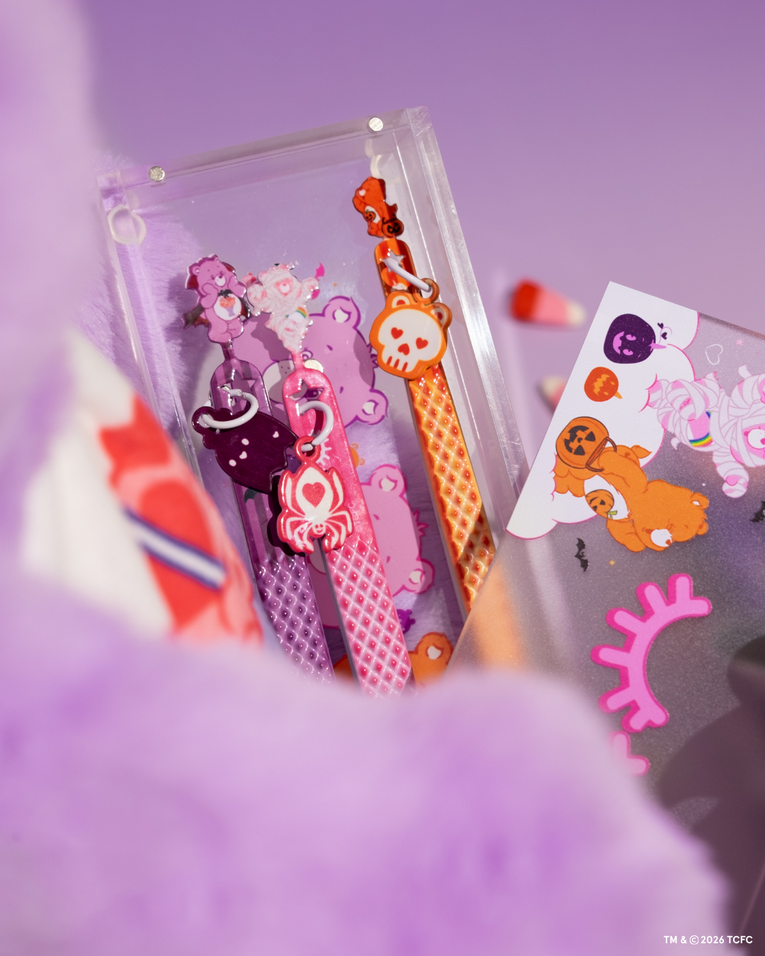 Élan Beauté x Care Bears Halloween tweezers in a clear magnetic case, featuring pink, purple, and orange designs with character charms, styled beside matching collection packaging.